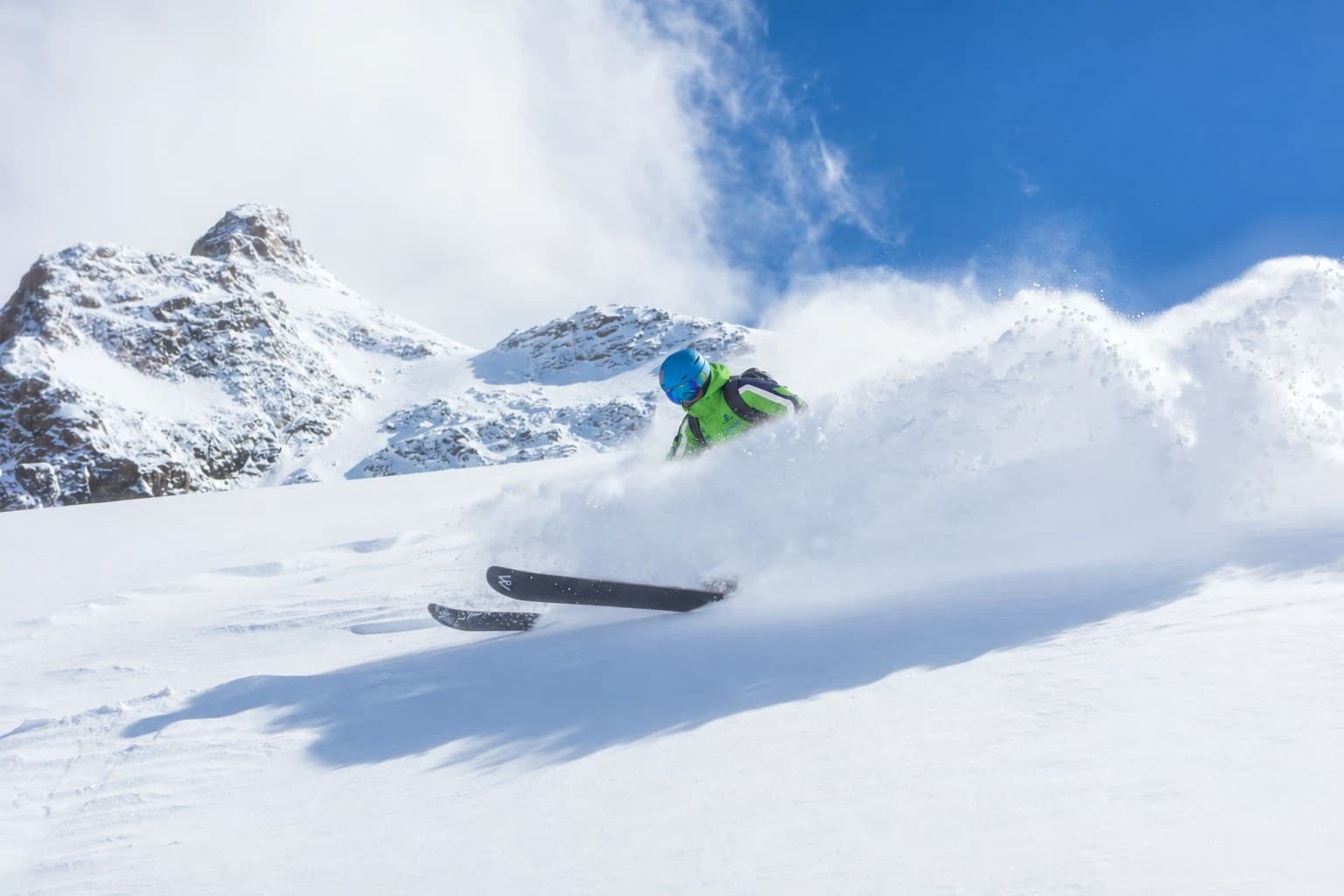 Lyžiar v zelenej bunde SKI EXPERTS v prašane pod horskými štítmi